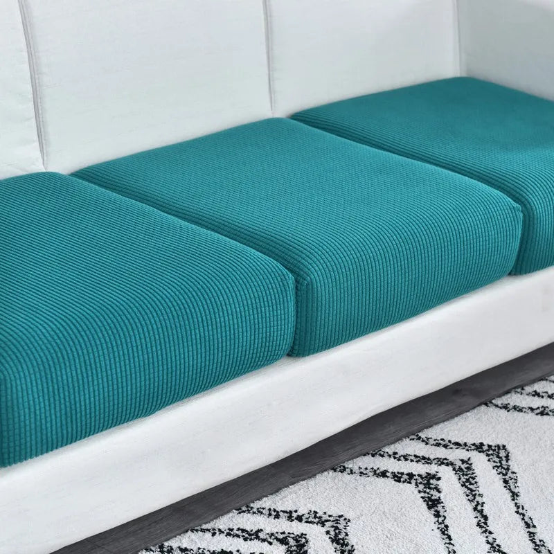 A white sofa seat cushion protector slipcover with teal fabric cushions on a gray floor.