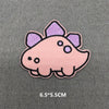 A pink and purple embroidered iron-on patch shaped like a stylized dinosaur head on a gray fabric background.
