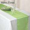 Elegant satin green table runner displayed on a white tablecloth with silverware and glassware.