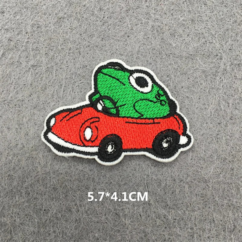 An embroidered patch featuring a green frog sitting on a red car.