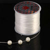 Spool of white stretchy beading thread with a decorative label and a strand unwound below.