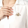 A close-up of a woman wearing a white collared shirt with a crystal bee brooch featuring a pearl accent.