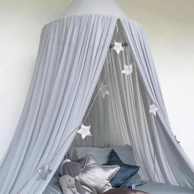 A light gray canopy mosquito net draped over a bed with soft pillows and star decorations.