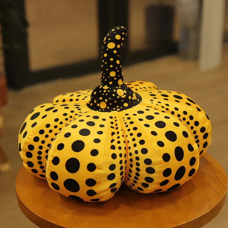 A yellow pumpkin plush cushion covered in black polka dots.