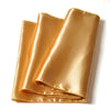 A golden satin table runner rolled and displayed on a white surface.