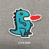 A blue dinosaur embroidered iron-on patch with a red tongue on a gray fabric background.