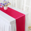 A pink satin table runner is displayed on a white tablecloth with a small bouquet of purple and yellow flowers.