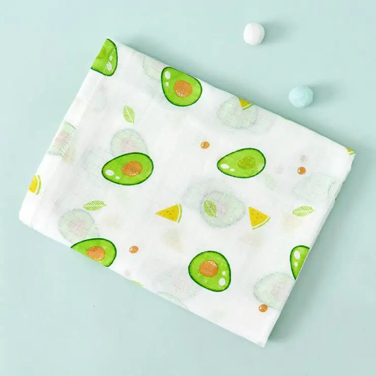 A white muslin swaddle blanket featuring green avocado-shaped prints on a light blue background.