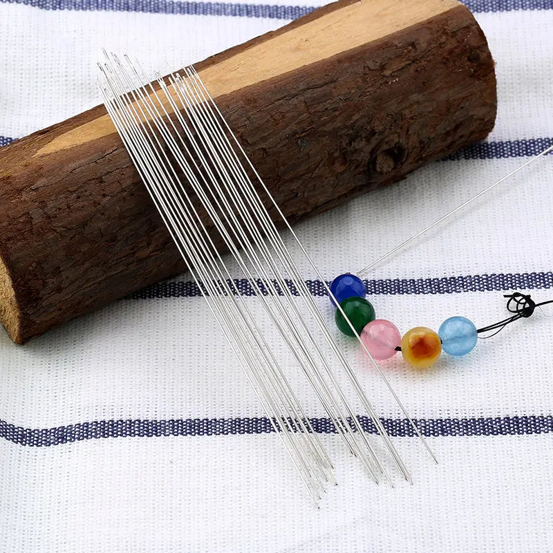 A set of precision stainless steel beading needles laid out on a wooden cylinder and white fabric.