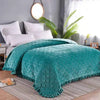 Teal crystal velvet quilted bedspread draped over a bed in a bright room.