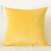 A square, solid yellow velvet decorative cushion cover resting on a white surface.