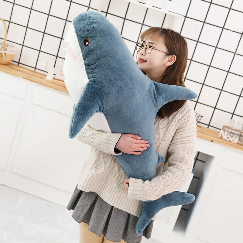 A young girl is hugging a large blue shark plush toy in a kitchen setting.