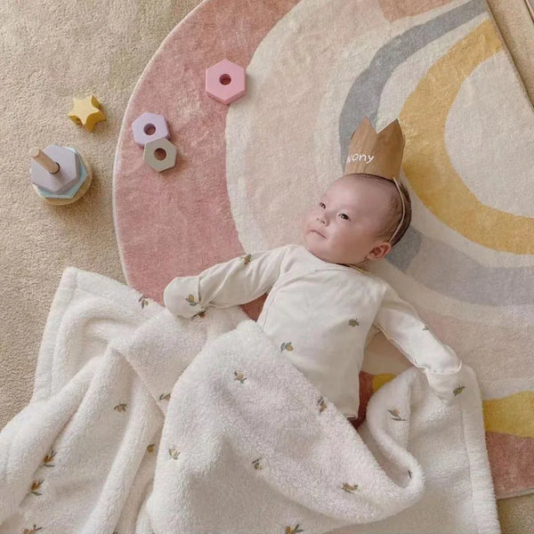 A newborn baby is lying on a pink and cream patterned blanket, wrapped in a white fleece blanket.