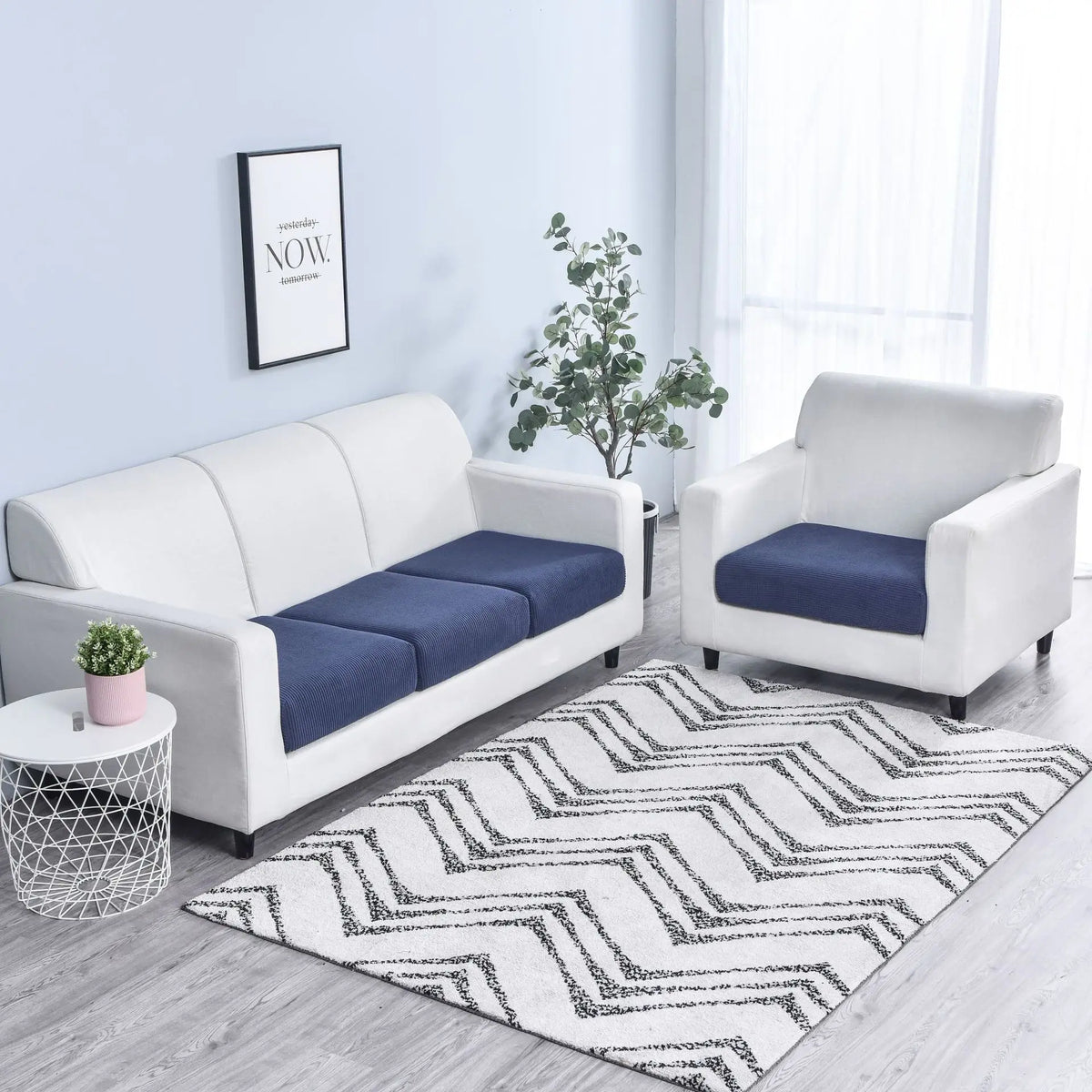 A white sofa and armchair set with dark blue seat cushion covers placed on a rug in a bright room.