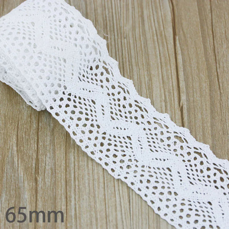 A close-up of a white cotton embroidered lace trim, showing its intricate pattern and texture.