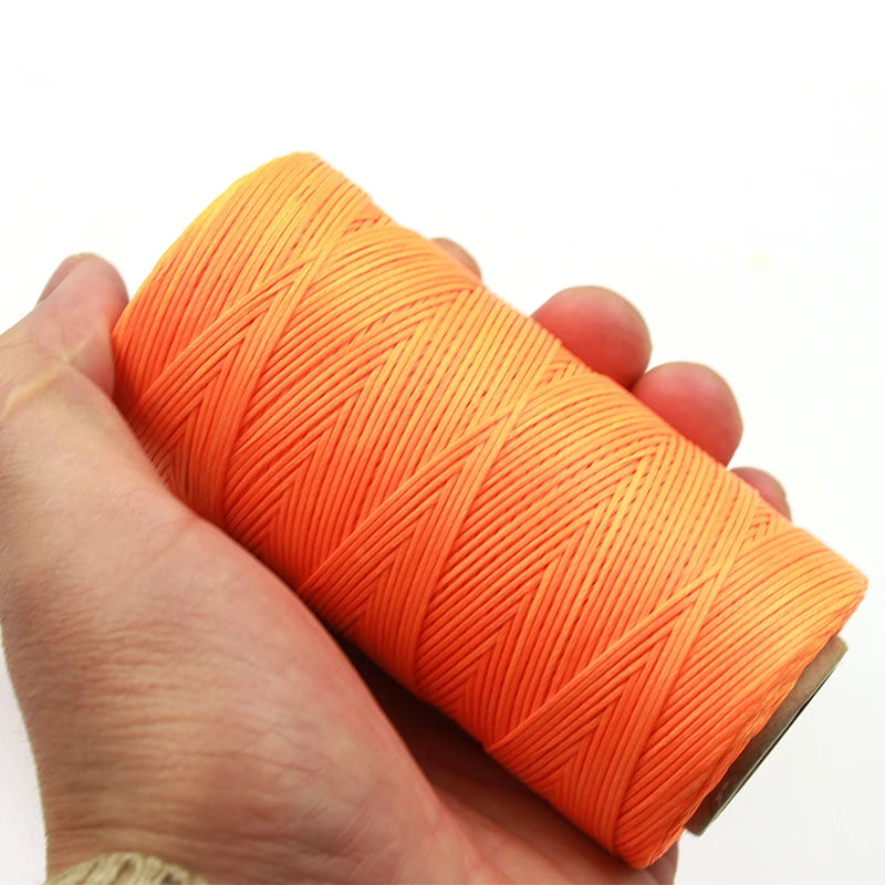A hand holds a spool of bright orange waxed thread for leather and crafting.