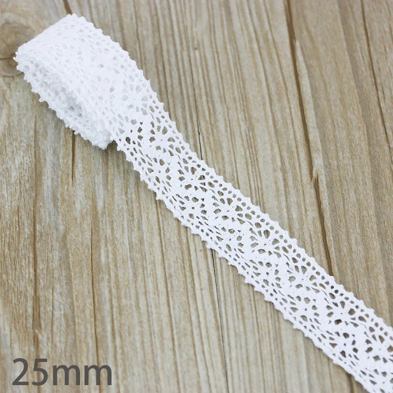 A white cotton embroidered lace trim with a delicate openwork pattern is shown on a wooden surface.
