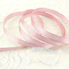 A roll of light pink satin gift ribbon showing multiple loops on a white lace background.