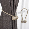 A close-up of a gray fabric curtain with beige magnetic pearl ball tiebacks.
