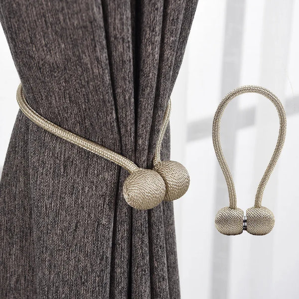 A close-up of a gray fabric curtain with beige magnetic pearl ball tiebacks.