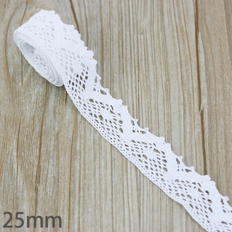 A white cotton embroidered lace trim is shown lying on a wooden surface.
