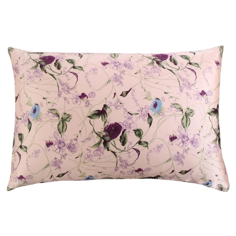 A square silk pillowcase with a pale pink background featuring a purple and green floral print.