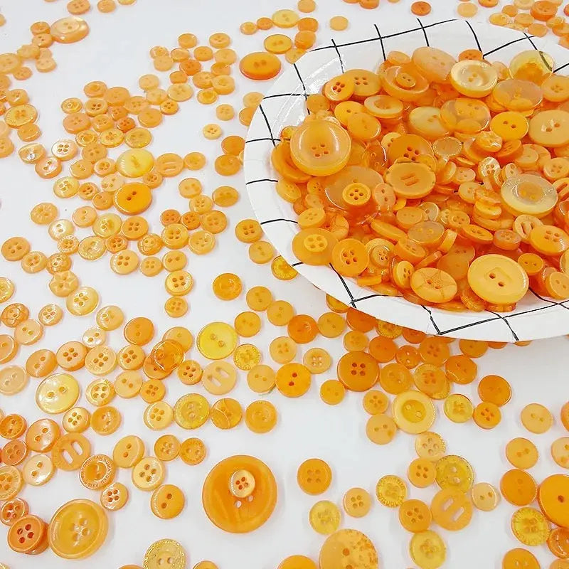 A pile of small, round wooden buttons in various shades of orange and yellow scattered on a white surface.