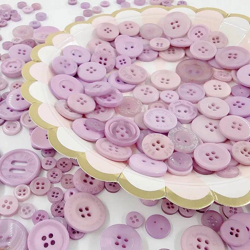 A collection of various sized wooden buttons in shades of pink and purple arranged on a white surface.