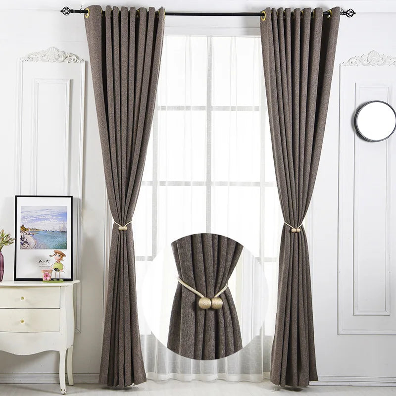 Two gray fabric curtains with magnetic pearl ball tiebacks hanging in a window.