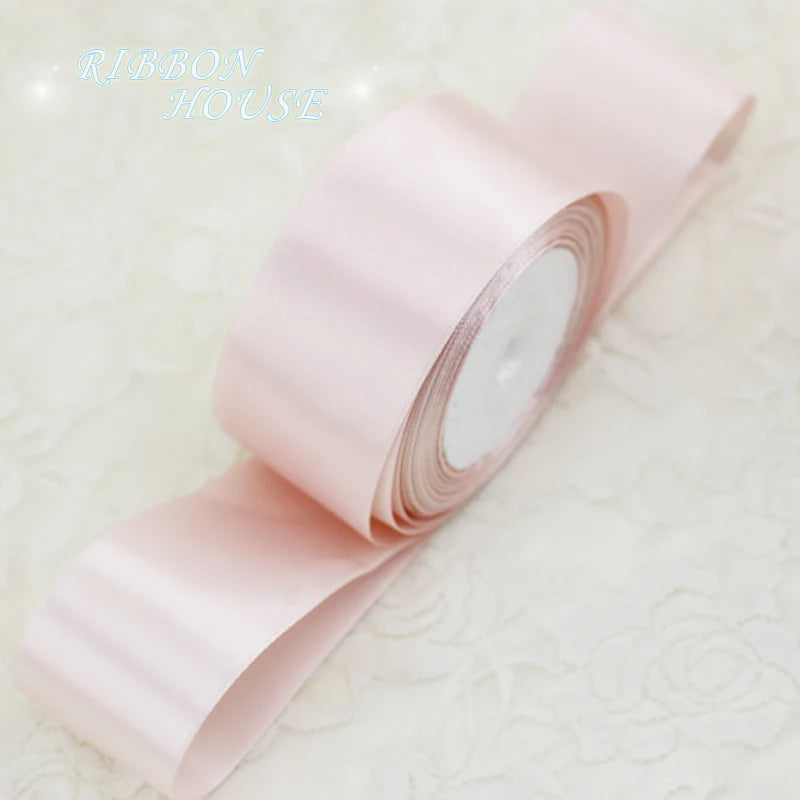 A roll of light pink satin gift ribbon, showing the smooth texture and white core.