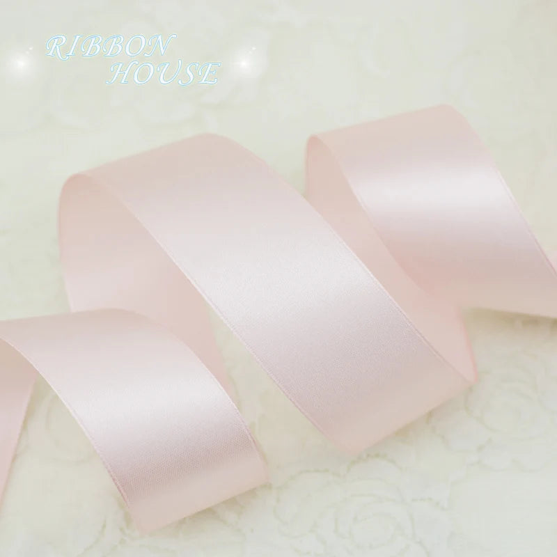 A roll of light pink satin gift ribbon lying on a white surface.