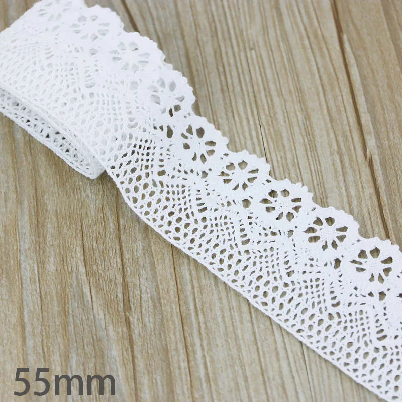 A close-up of white cotton embroidered lace trim laid diagonally on a wooden surface.
