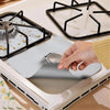 A hand places a silver cleaning mat onto a black gas stove grate for cleaning.