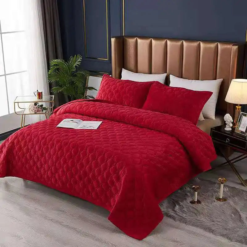 A vibrant red crystal velvet quilted bedspread draped over a bed with a brown upholstered headboard.