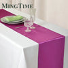 Elegant purple satin table runner displayed on a white tablecloth with glassware and a green napkin.
