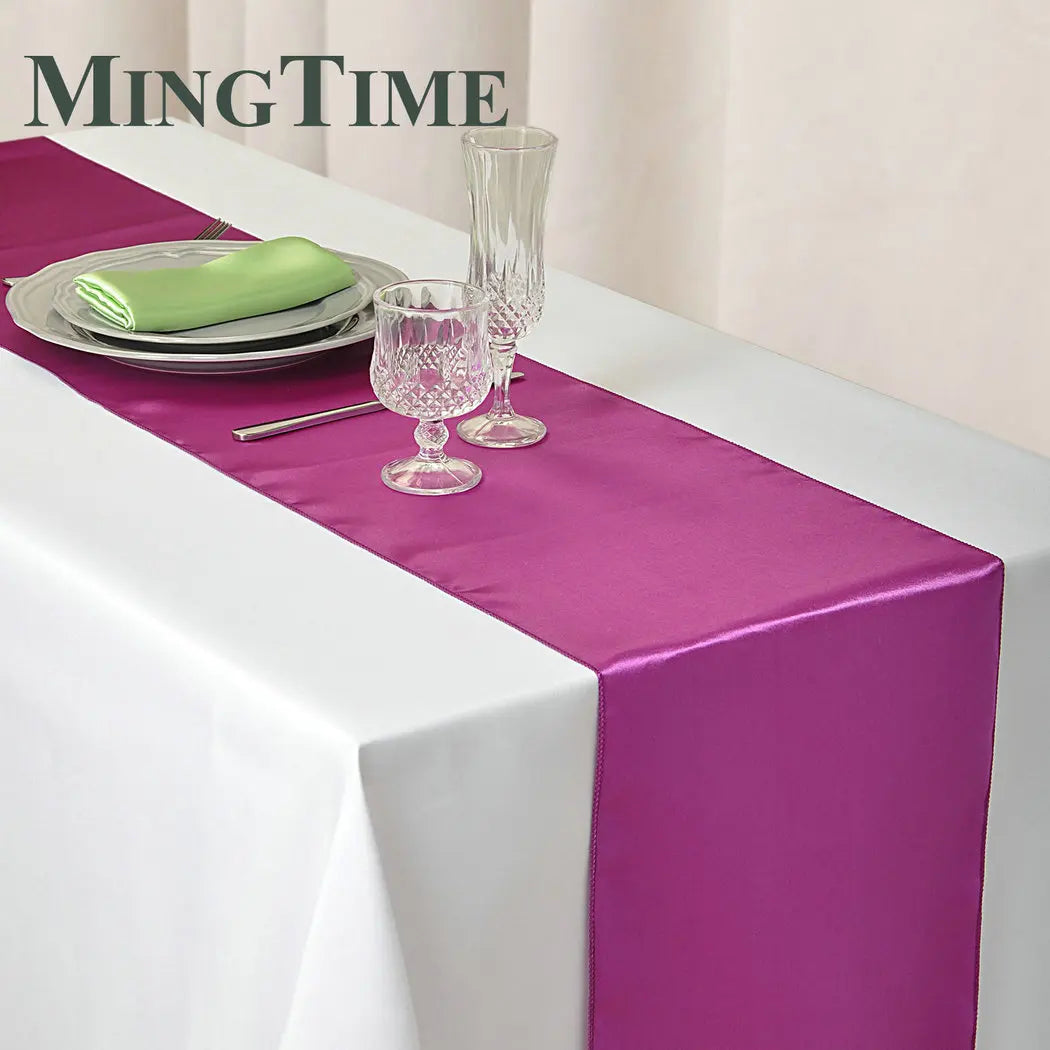 Elegant purple satin table runner displayed on a white tablecloth with glassware and a green napkin.