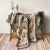 A bohemian geometric throw blanket in beige and rust tones draped over a wooden chair.