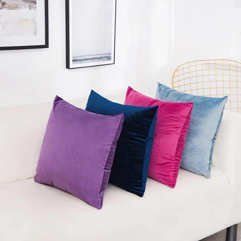 A collection of solid velvet decorative cushion covers in shades of purple, blue, and pink arranged on a white sofa.