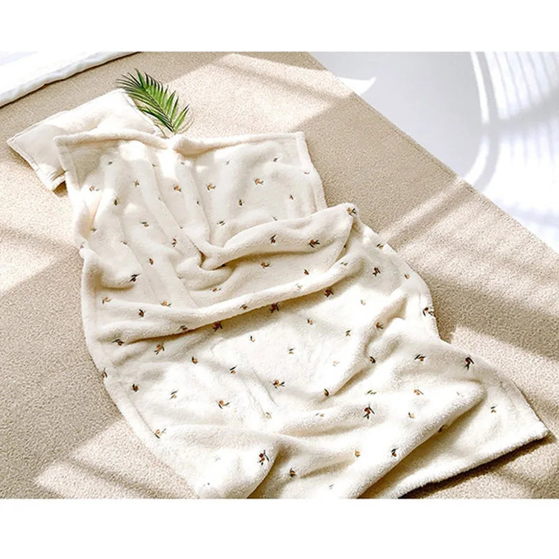 A soft cream coral fleece flannel blanket with small leaf patterns is draped on a light beige surface.
