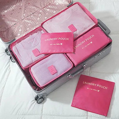 A silver suitcase is open, displaying a pink laundry pouch organizer set with six individual pouches.