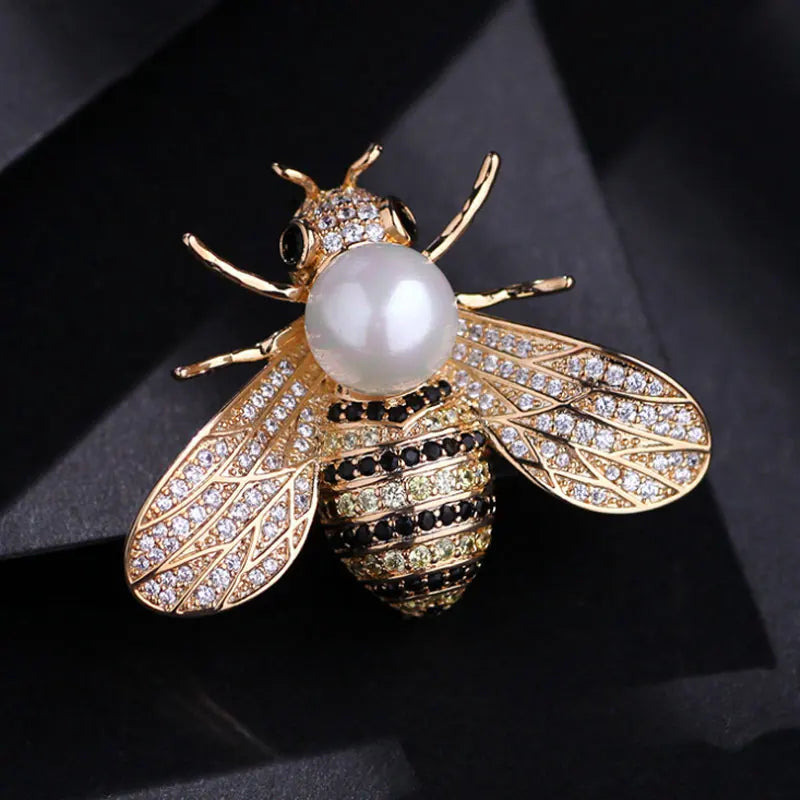 A gold-toned crystal bee brooch featuring a pearl accent and detailed wing design.