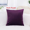 A dark purple velvet decorative cushion cover resting on a white sofa.