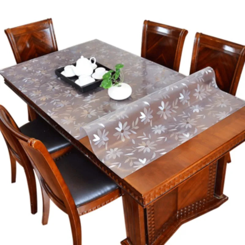 A wooden dining table set with chairs and a transparent PVC tablecloth.