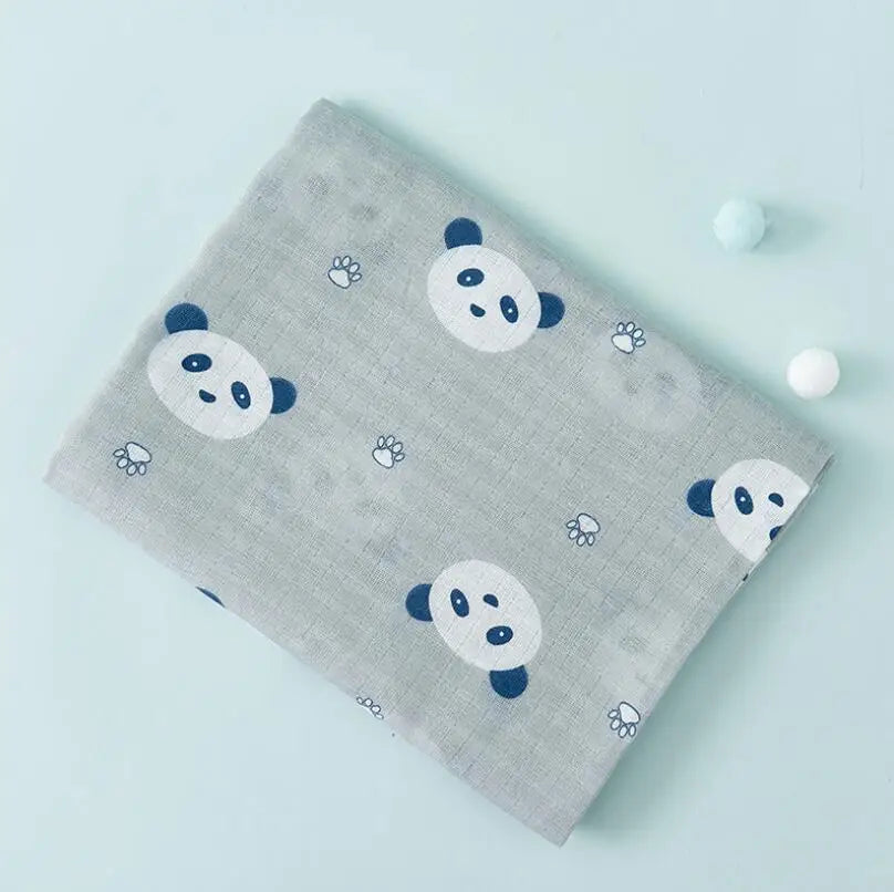A gray muslin swaddle blanket patterned with white panda faces and paw prints, placed on a light blue surface.