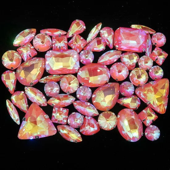A collection of pink and orange faceted rhinestones and gemstones scattered on a black background.