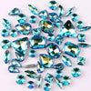 A collection of 50 sparkling blue and green silver claw rhinestones scattered on a white background.