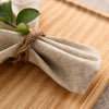 A bundle of natural linen table linens tied with twine, featuring green leaves.