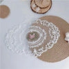 A round woven coaster with an oval white lace embroidery and a natural wood slice nearby.