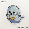 A light blue embroidered patch of a smiling, blob-like creature with pink accents.