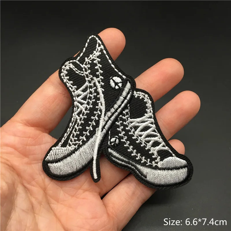 Pair of black embroidered punk style boots or shoes shown held in a hand